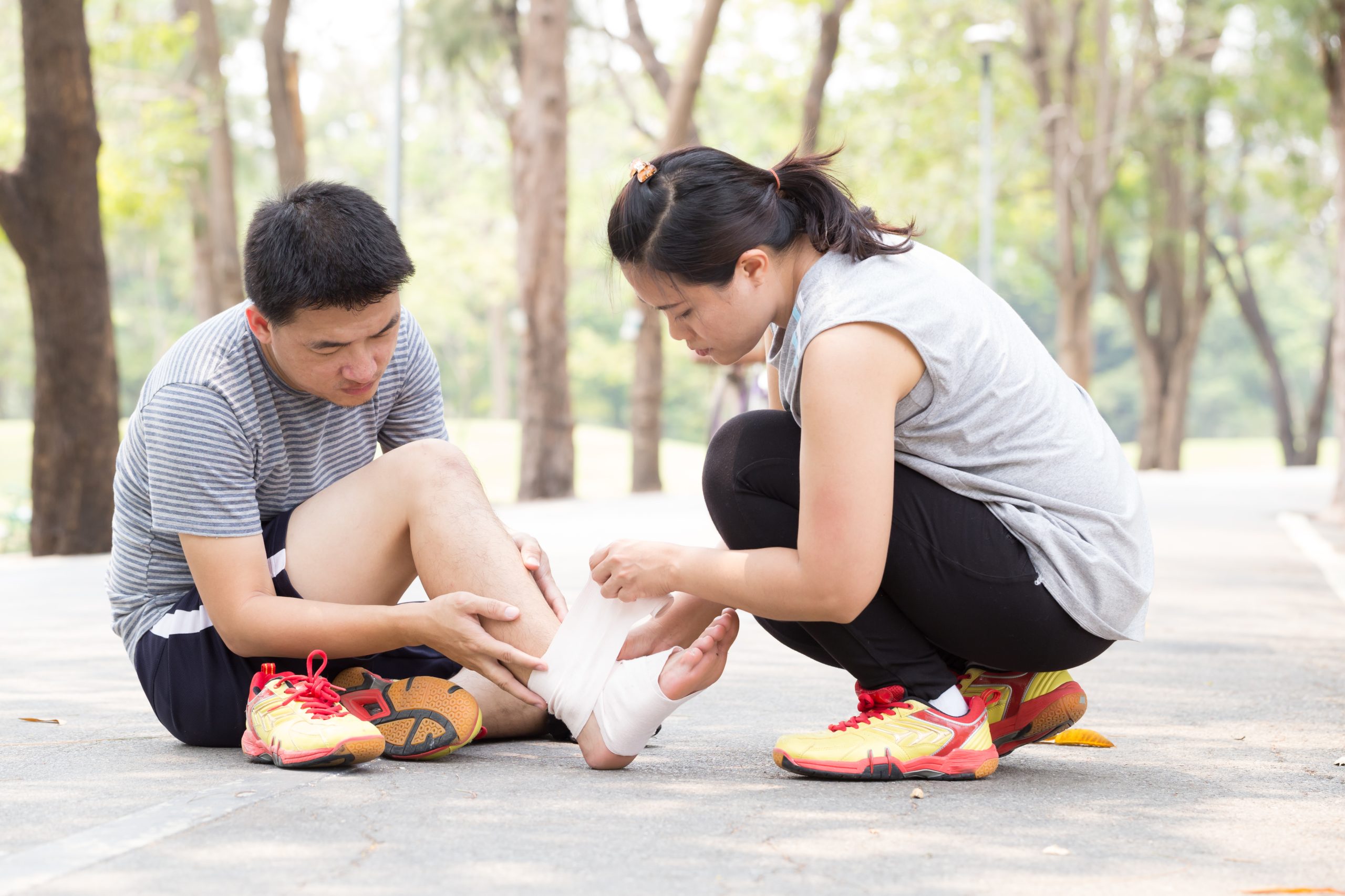 Sports injury. Man with twisted sprained ankle and getting help from woman bandaged ankle