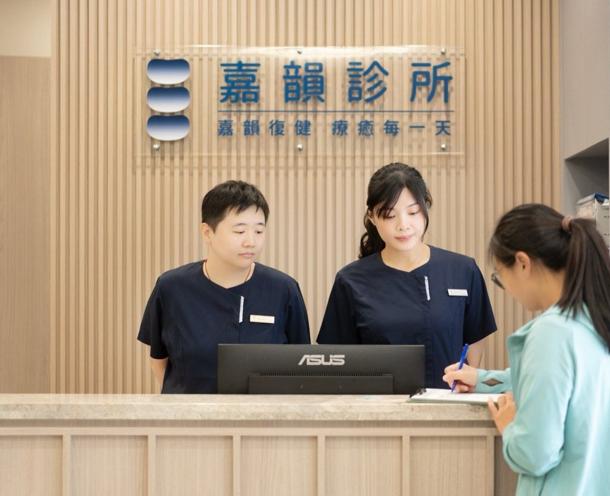 嘉韻診所櫃檯,兩位護理人員在診所招牌前協助一位病人填寫初診資料